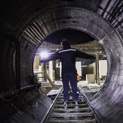 male confined underground tunnel of heating duct with rusty tubes and rail